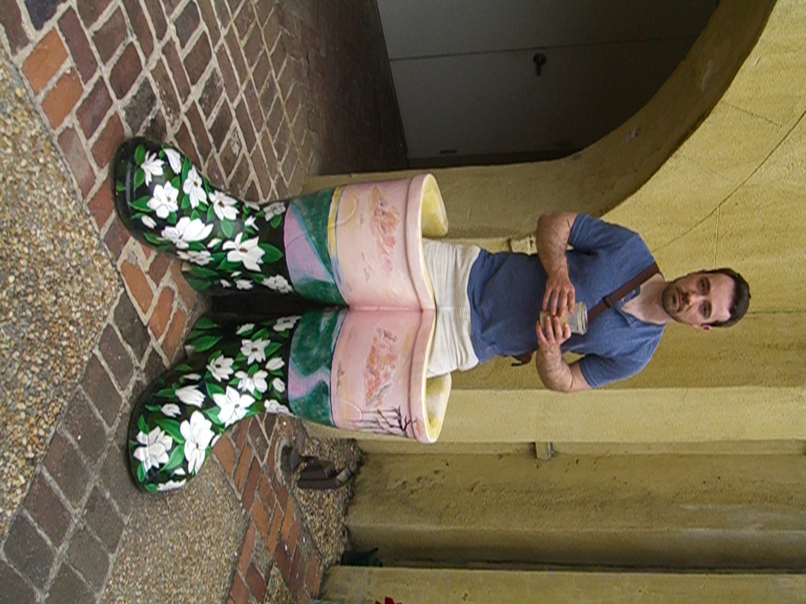 Man posing through a large decorative painted boot sculpture outdoors